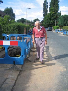 photograph of an older person having to walk on the road due to streetworks on the footway